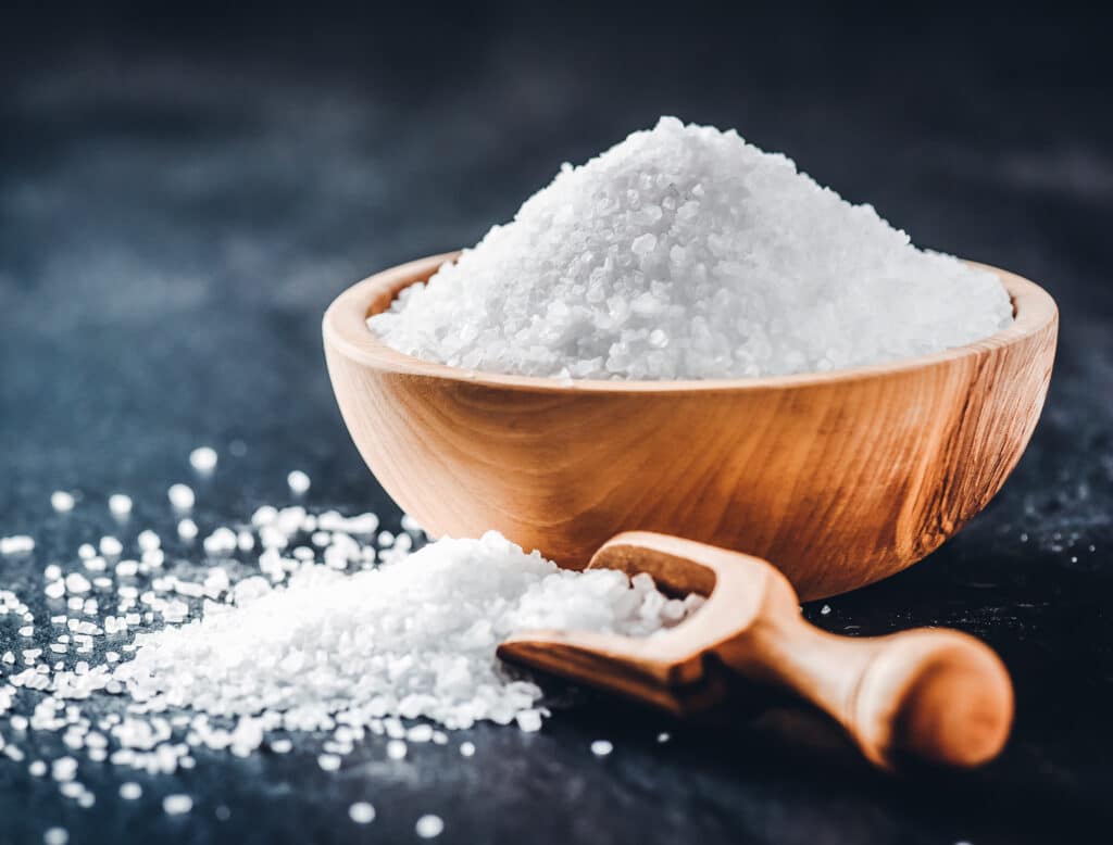 Salt in wooden scoop on dark stone table.