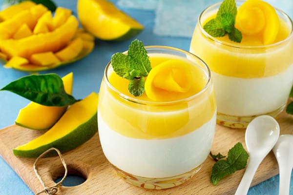 Mango-Dessert in Gläsern mit gestückelter Mango im Hintergrund