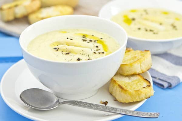 Spargelcremesuppe in einer tiefen Schüssel, angerichtet mit zwei Stücken Brot und Löffel auf einem Unterteller